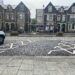 Buildings in the background and bus stops. There are diagonal blue badge parking bays. There are hatched areas on each side of the bay. The curb is high behind the bay with drop curbs on either side.